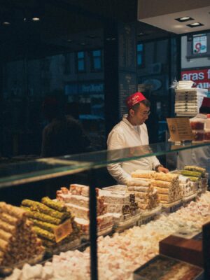 Man selling traditional Middle Eastern sweets at an indoor market stall.